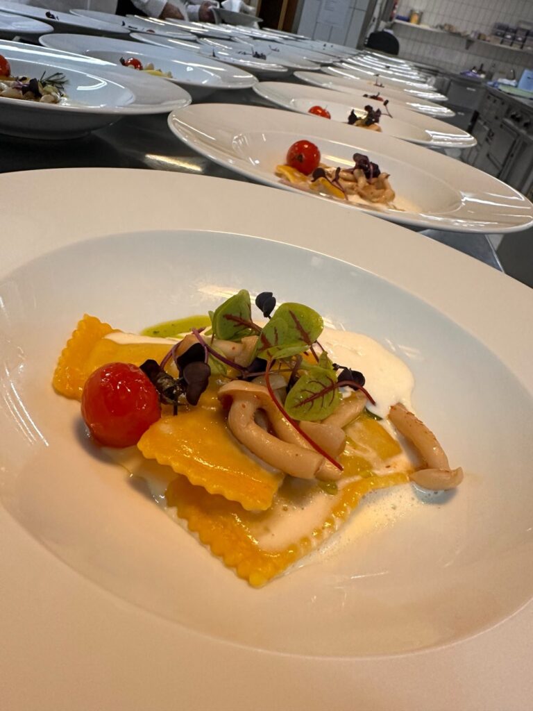 Frisch angerichtete Ravioli mit Pilzen, Kirschtomaten und Kräutern, viele Teller in Reihe in der Küche von ID Catering